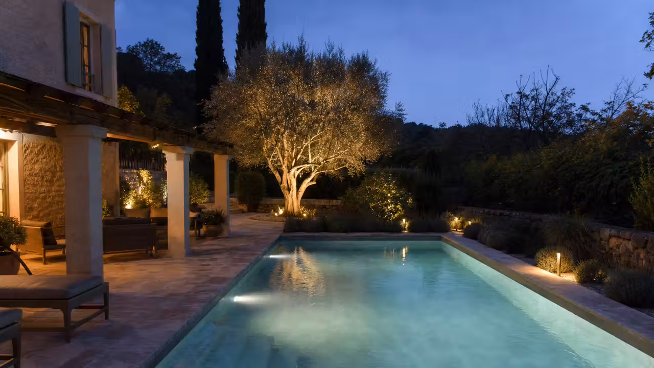 Piscine contemporaine éclairée la nuit, avec spots immergés, terrasse balisée et arbre mis en lumière