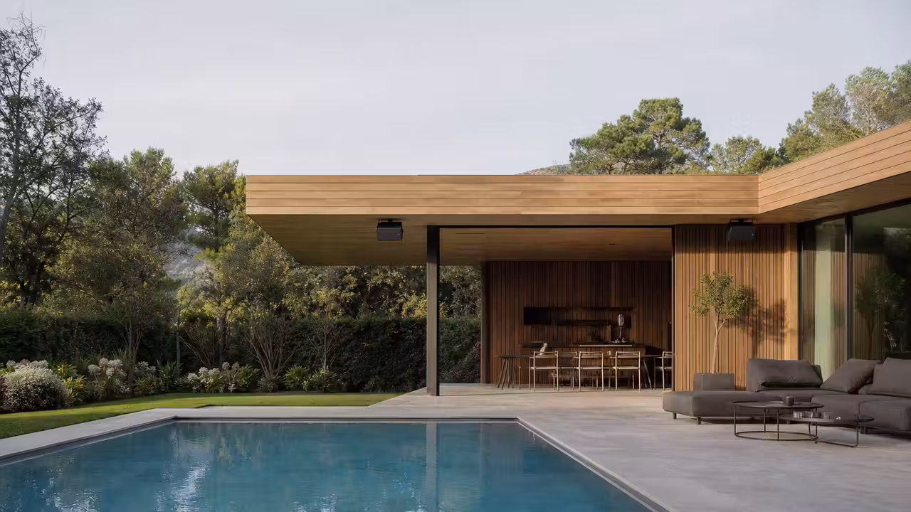 Enceintes extérieures discrètes installées sous un pool house face à une piscine et à sa terrasse.
