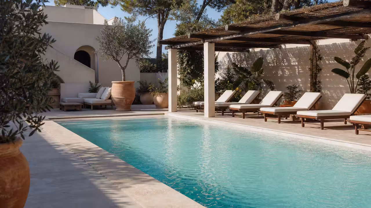 Terrasse de piscine méditerranéenne aux tons sable, pergola ajourée, végétation sobre et eau lumineuse