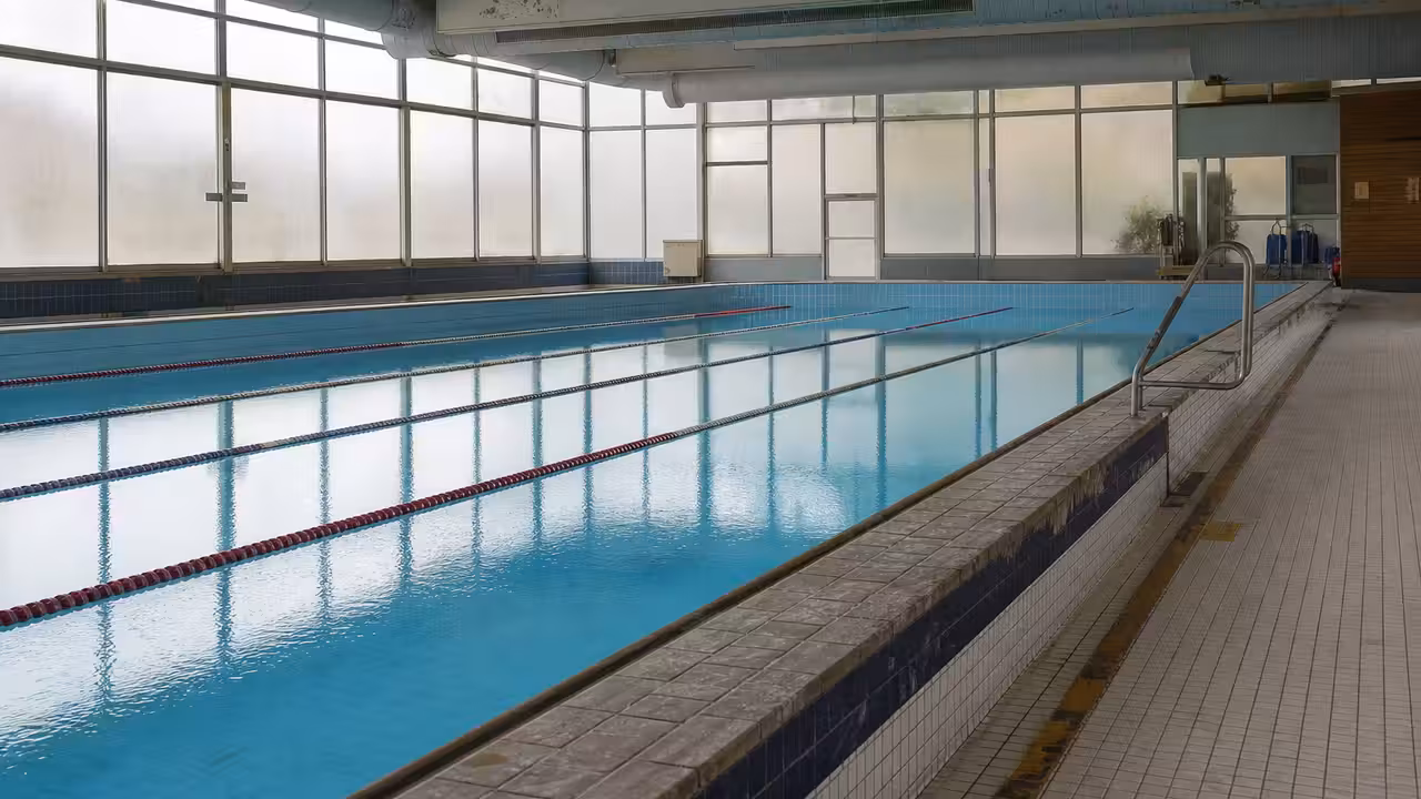 Entrée fermée d’une piscine municipale française, avec bassin couvert visible derrière les baies vitrées