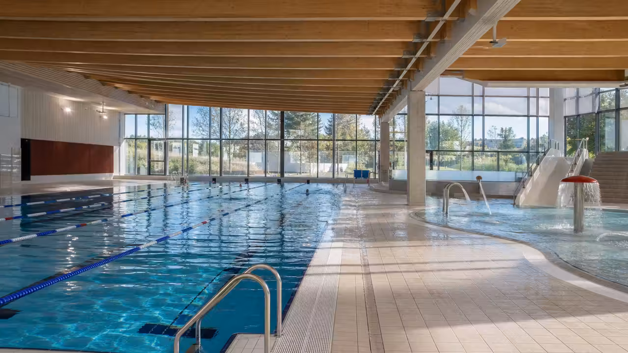 Vue intérieure d’un centre aquatique moderne avec bassin de nage, espace ludique et lumière naturelle.