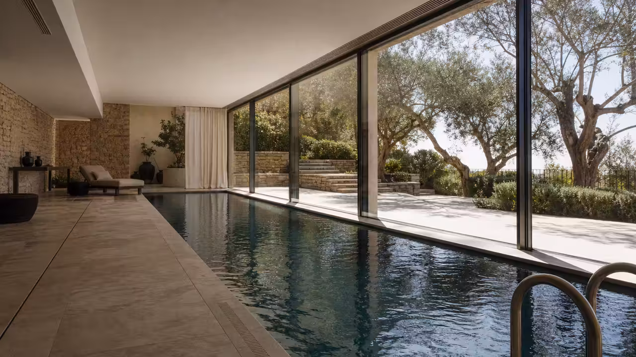 Piscine intérieure contemporaine avec baies vitrées, plafond ventilé et vue sur un jardin méditerranéen