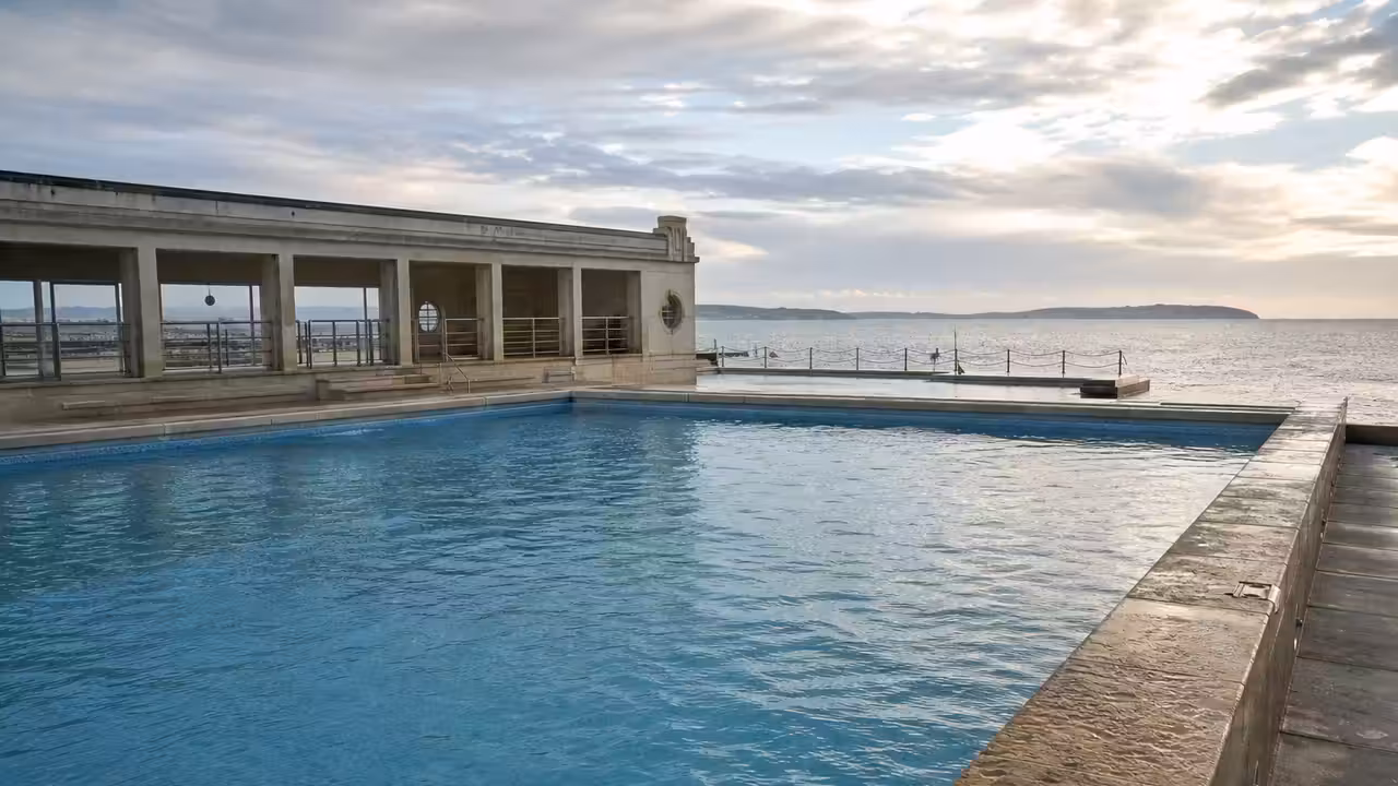 Bassin contemporain en bord de mer, revêtu de mosaïque claire et bordé de pierre minérale patinée