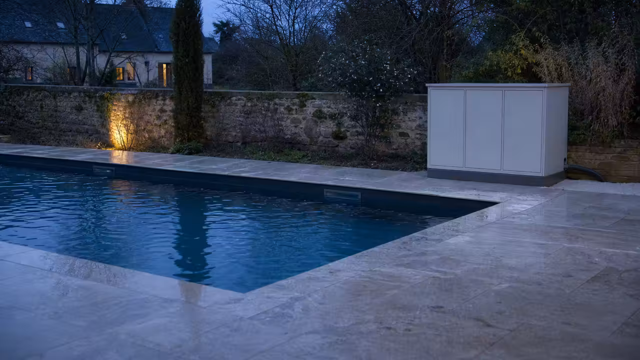 Local technique de piscine avec coffret électrique fermé et éclairage du bassin éteint au crépuscule