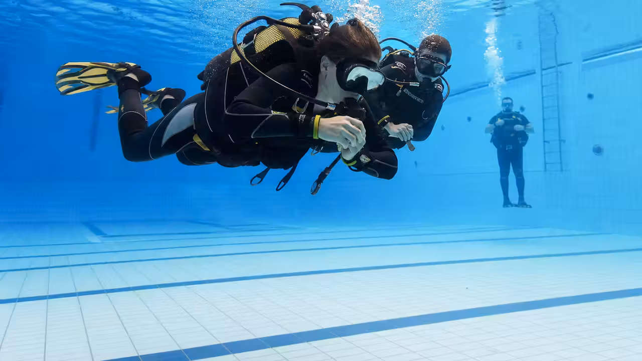 Deux plongeurs équipés s’exercent à la flottabilité dans le bassin d’une piscine couverte.