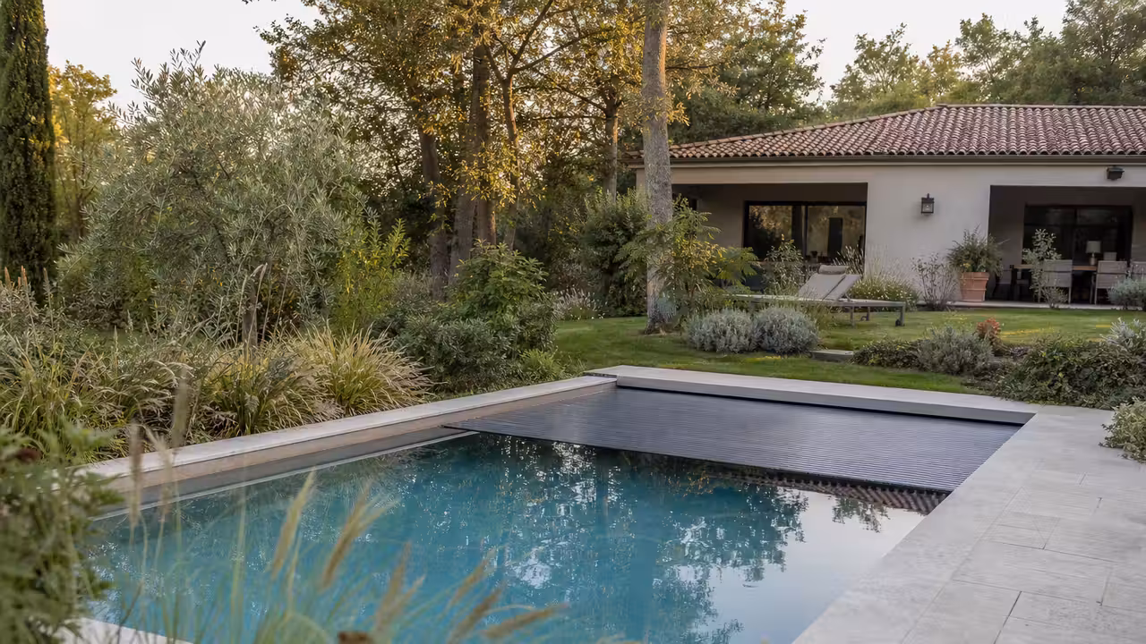 Piscine familiale compacte couverte dans un jardin contemporain, avec terrasse minérale et végétation sobre