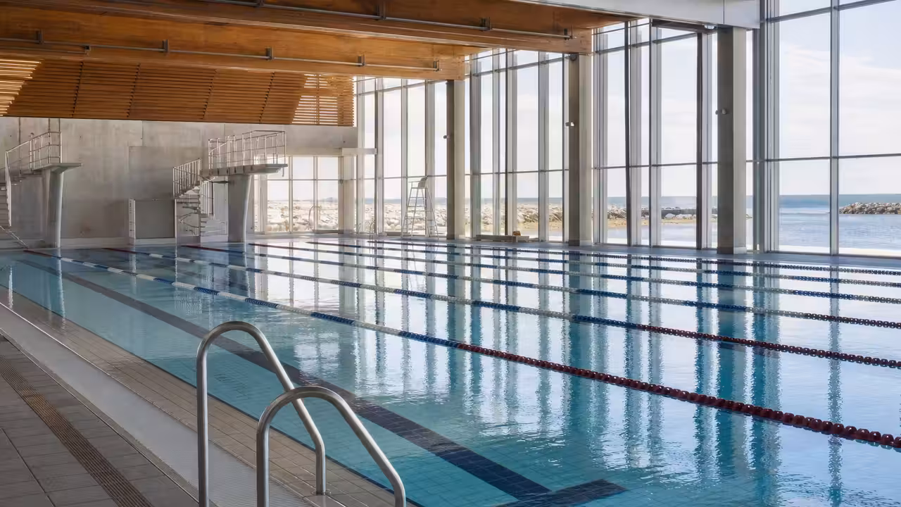 Vue d’un bassin municipal couvert de 25 mètres, avec lignes d’eau, baies vitrées et surveillance discrète