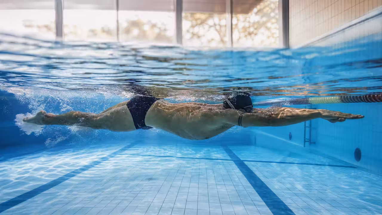Nageur vu de côté sous l’eau, en position allongée, dans un couloir de piscine baigné de lumière