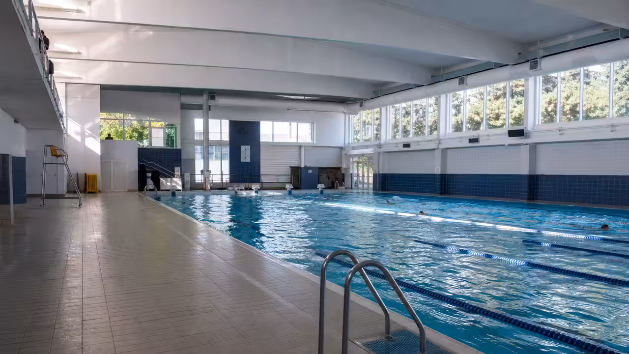 Bassin couvert d’une piscine publique avec lignes d’eau, gradins vides et lumière naturelle latérale