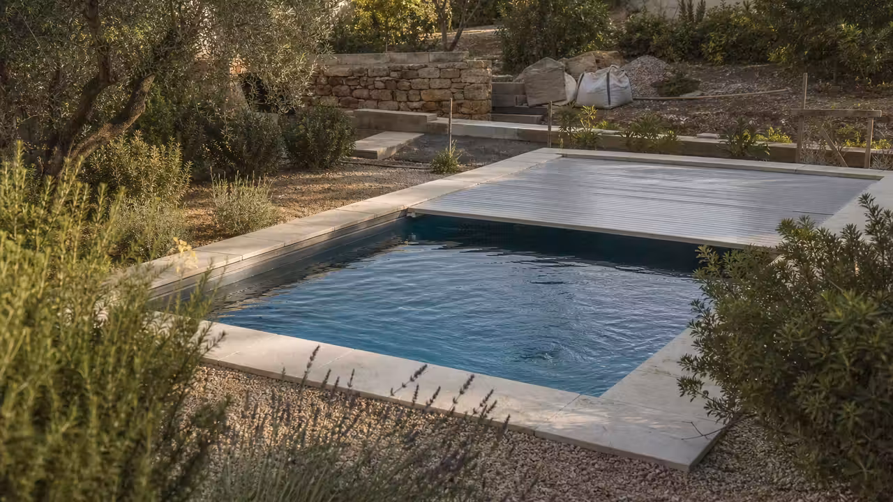 Piscine compacte couverte dans un jardin méditerranéen sec, avec chantier de maçonnerie en arrière-plan