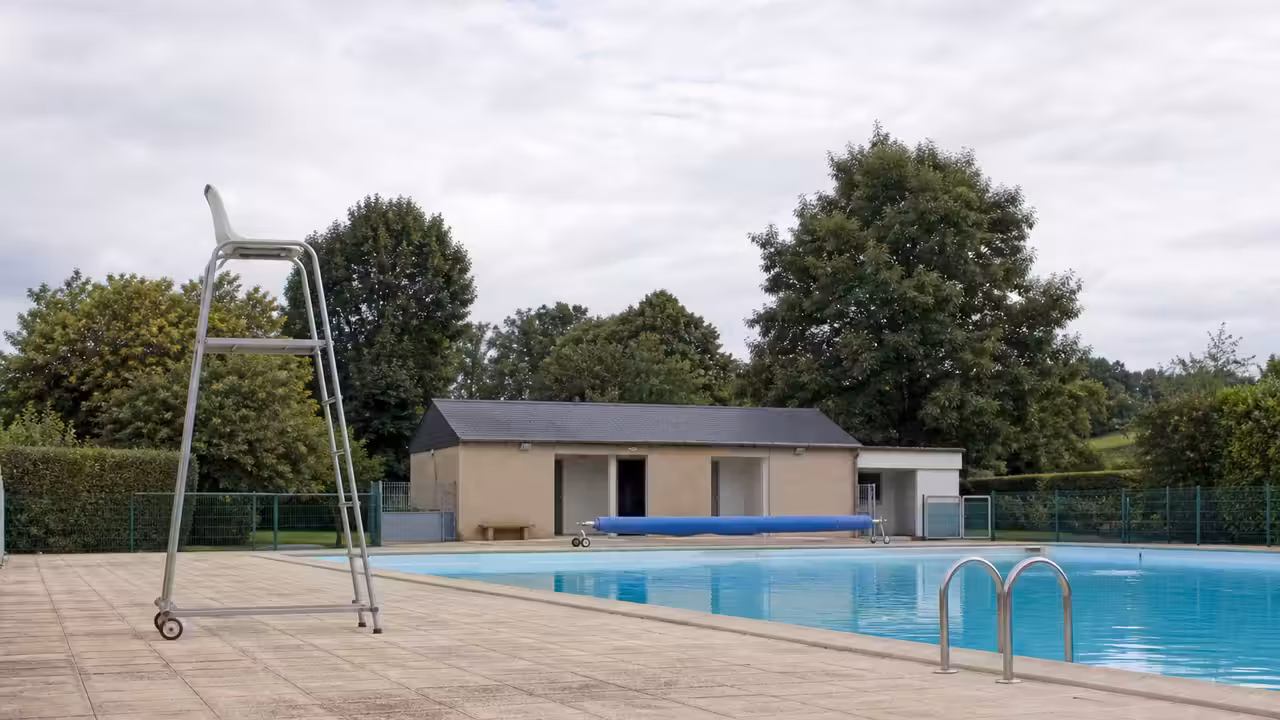 Bassin calme d’une piscine communale entouré de végétation normande, avant l’arrivée des baigneurs