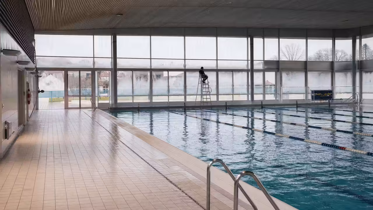 Bassin couvert municipal calme en hiver, avec lignes d’eau, gradins et lumière naturelle en arrière-plan