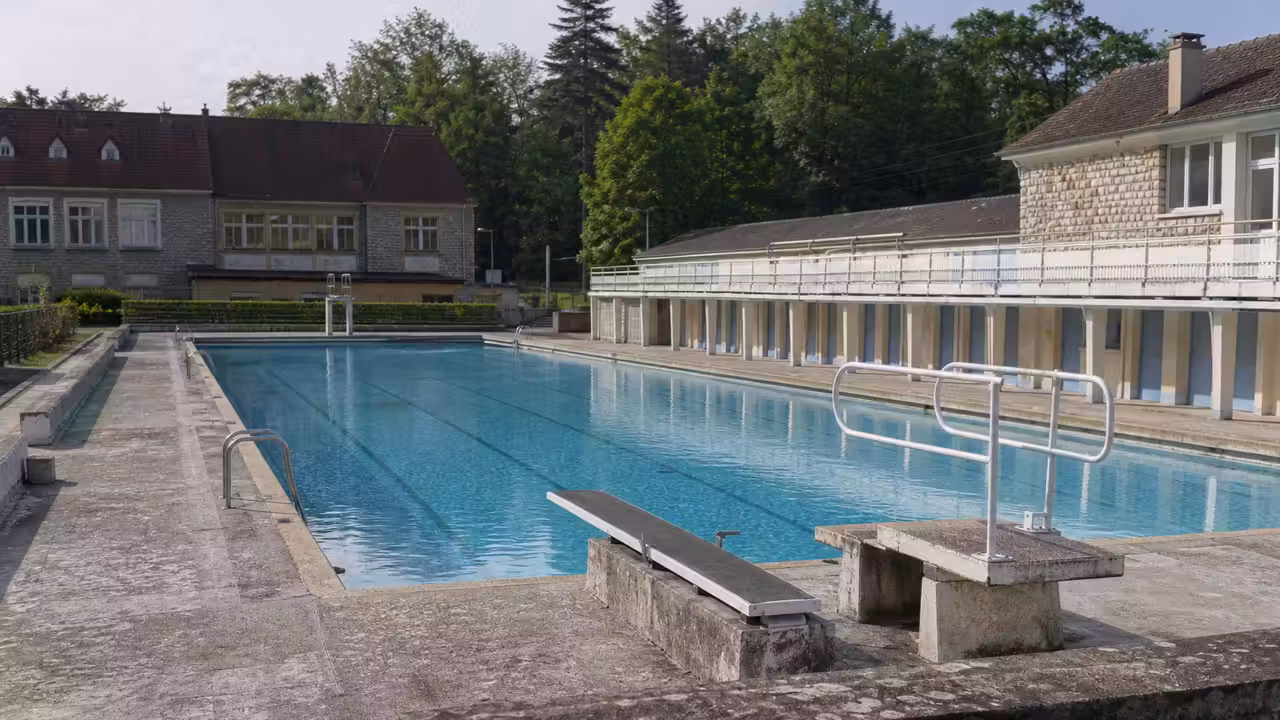 Bassin municipal extérieur en longueur, plages minérales et plongeoir, dans une petite ville jurassienne
