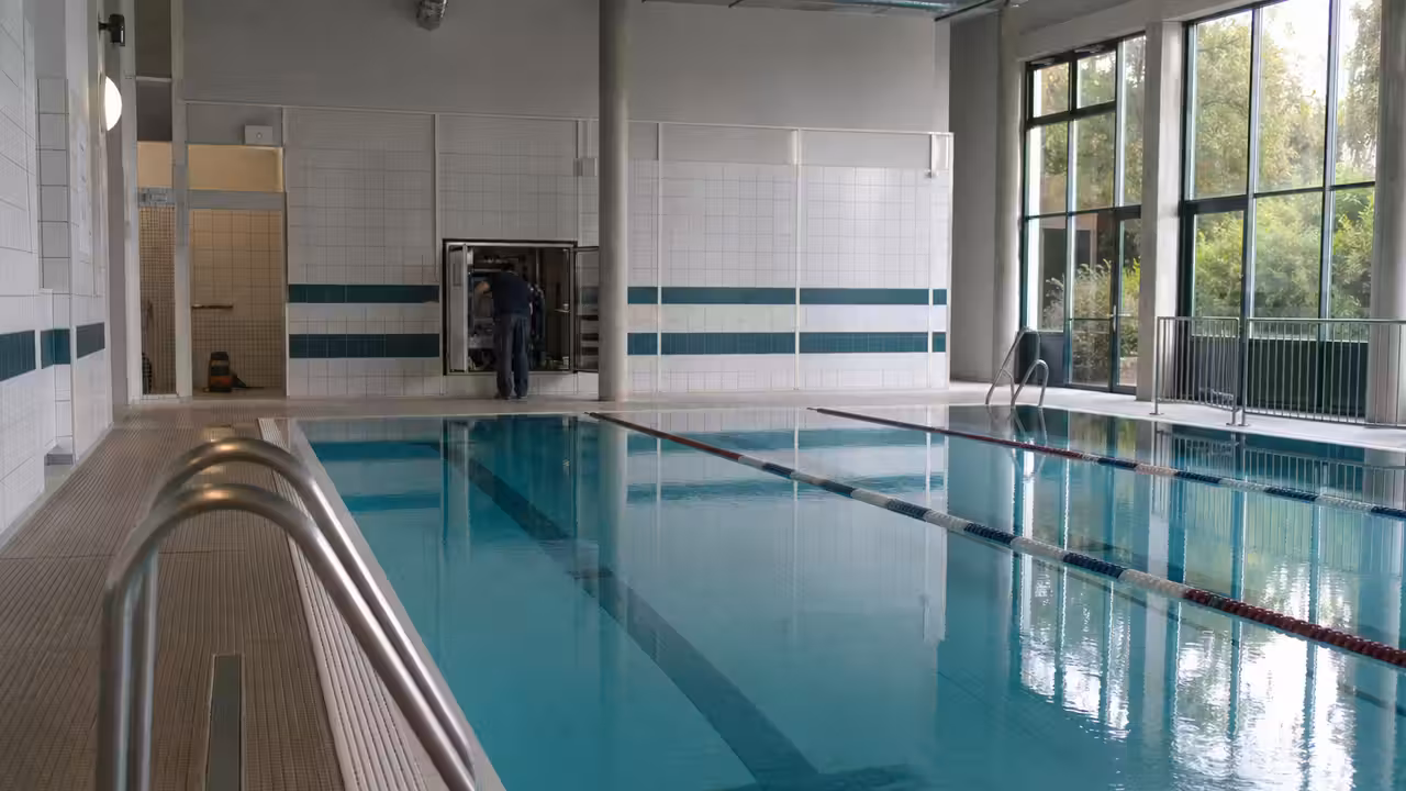 Bassin sportif vide dans une piscine municipale, avec couloirs de nage et matériel technique en intervention