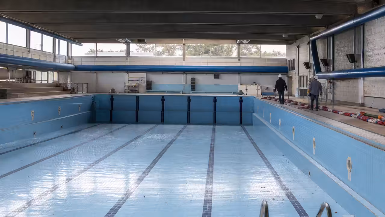 Entrée fermée d’un centre aquatique municipal avec bassin intérieur visible à travers les baies vitrées