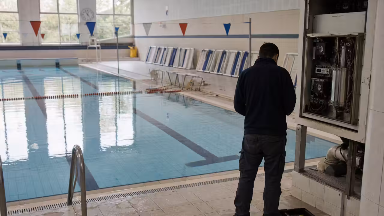 Bassin intérieur municipal vide, lignes d’eau retirées et panneau de fermeture temporaire à l’entrée