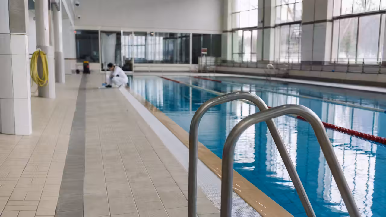 Bassin municipal intérieur vide pendant un contrôle sanitaire, avec lignes d’eau et lumière du jour