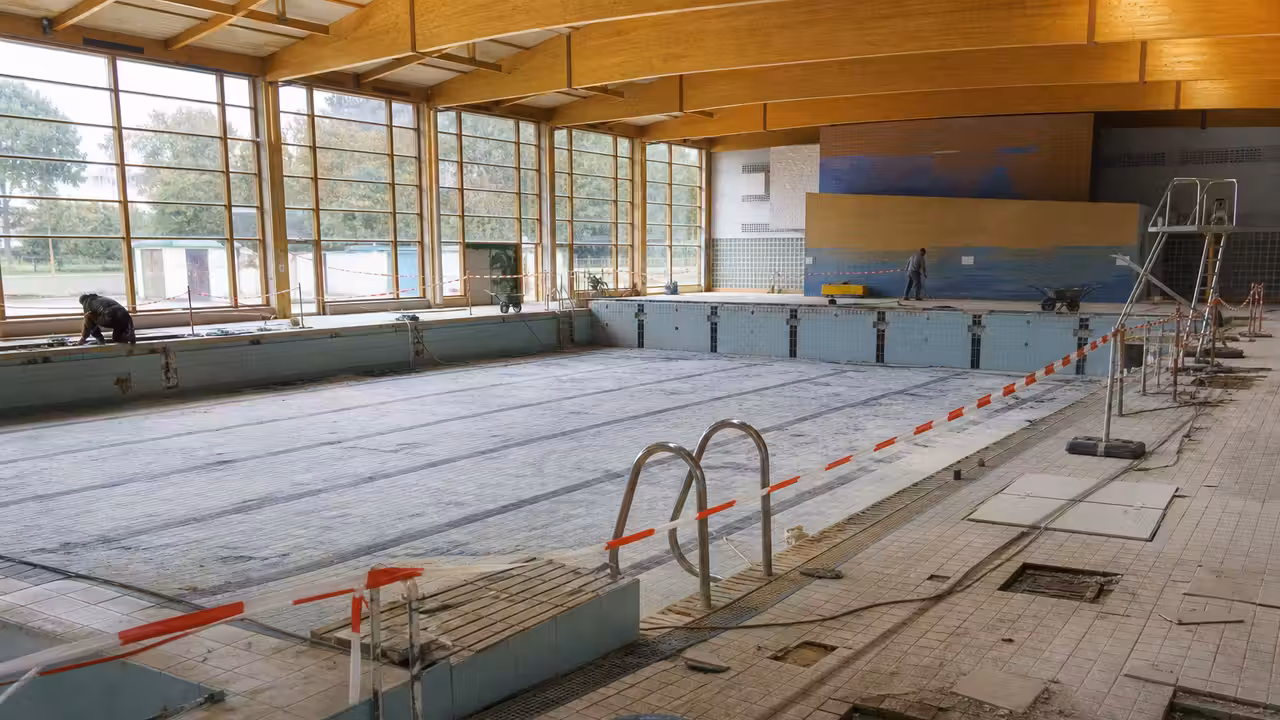Bassin couvert de piscine publique vide pendant des travaux de rénovation, avec plages carrelées et équipements techniques