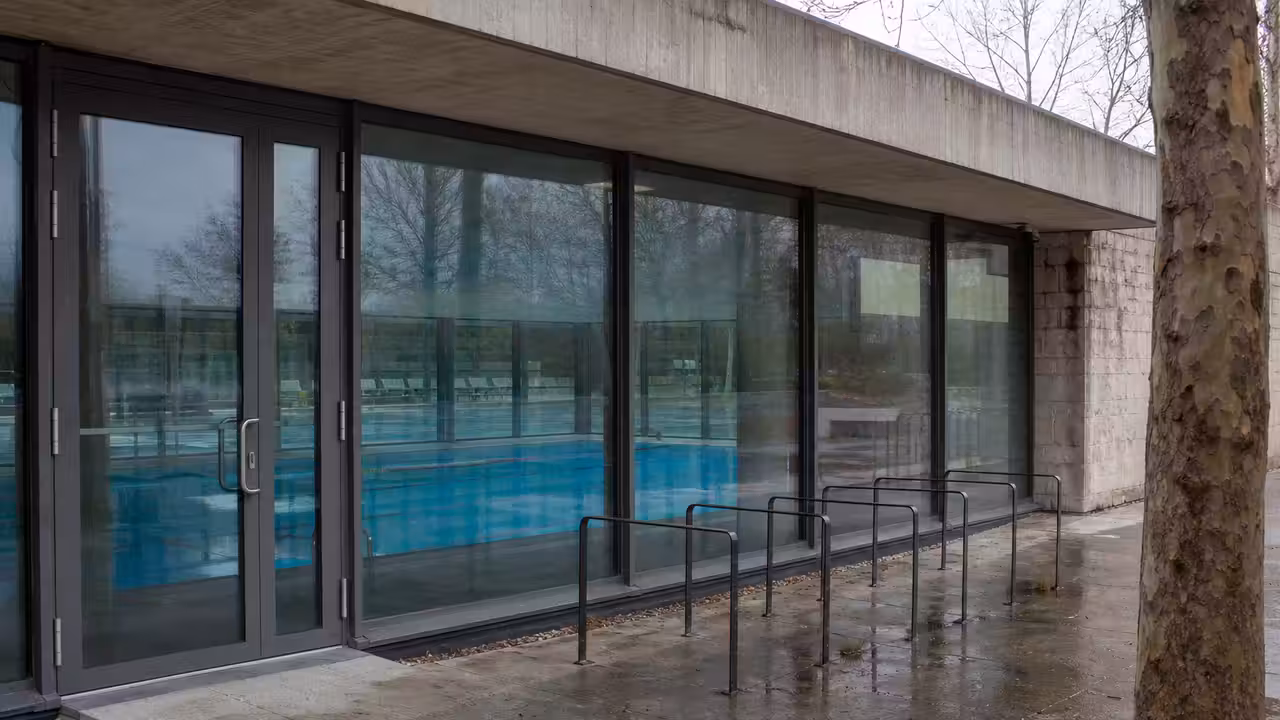 Entrée fermée d’une piscine municipale avec bassin couvert visible à l’arrière-plan, sans usagers