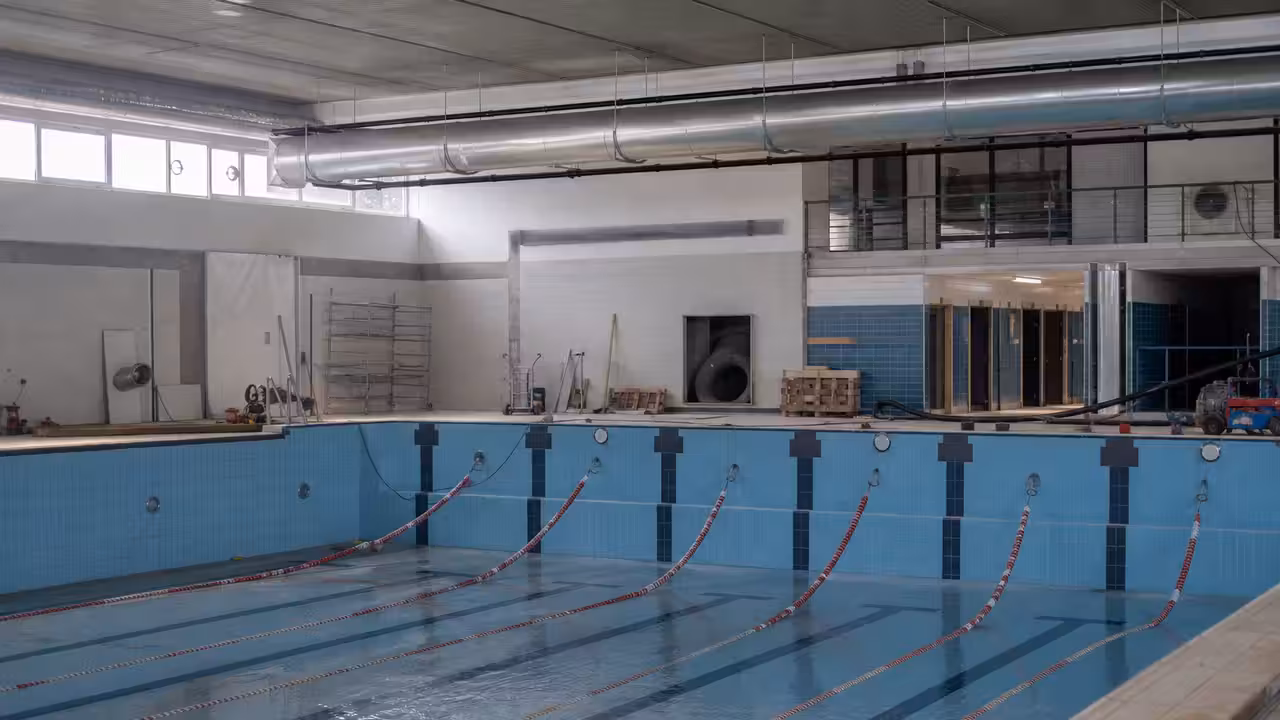 Bassin intérieur d’un centre aquatique public avec lignes d’eau, gradins et grandes baies vitrées