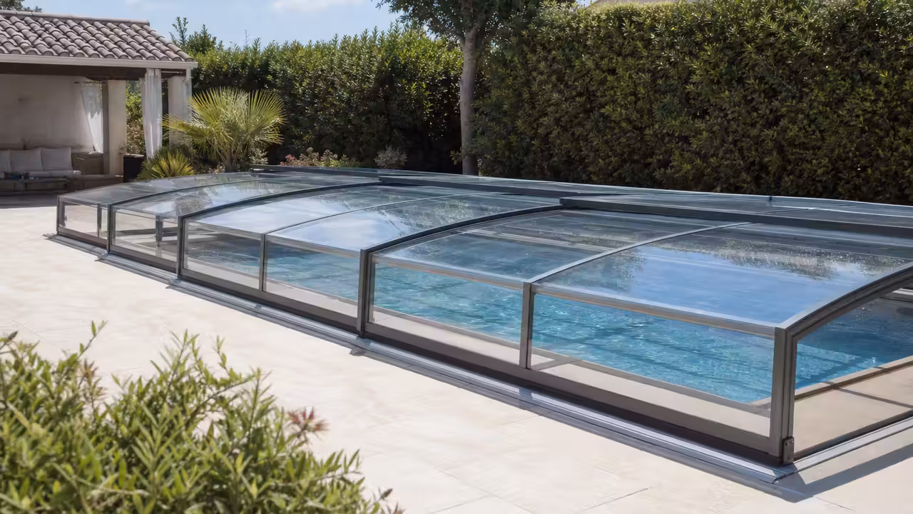 Abri télescopique bas installé sur une piscine de jardin, avec terrasse et végétation en arrière-plan
