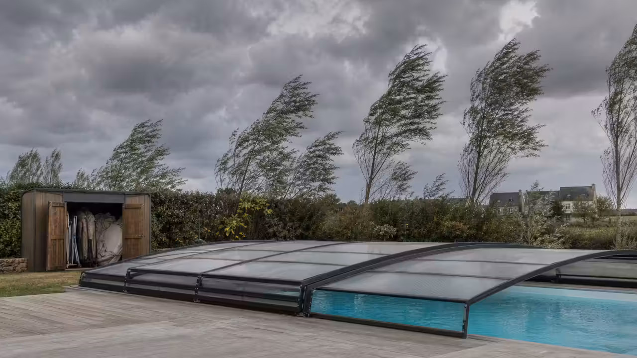 Piscine de jardin sécurisée avant une tempête, avec mobilier rangé et abri fermé sous un ciel venteux