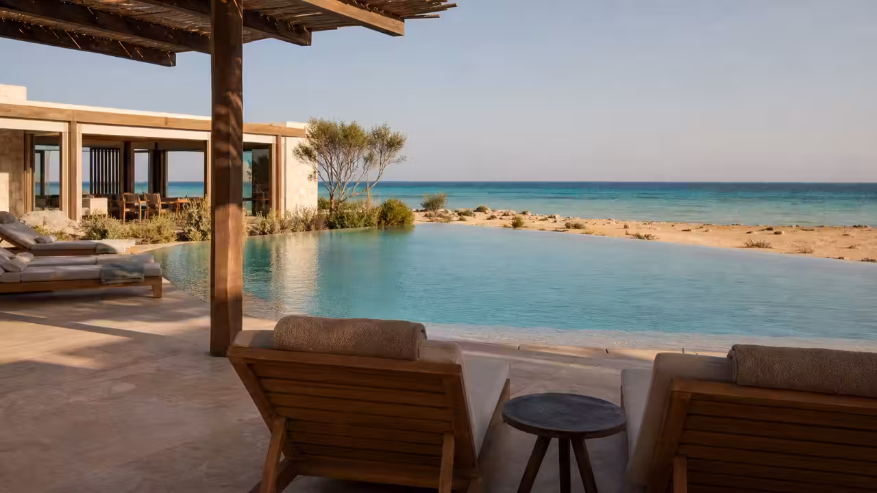 Bassins paysagers d’un resort en bord de mer, entre végétation sèche, plage et horizon marin