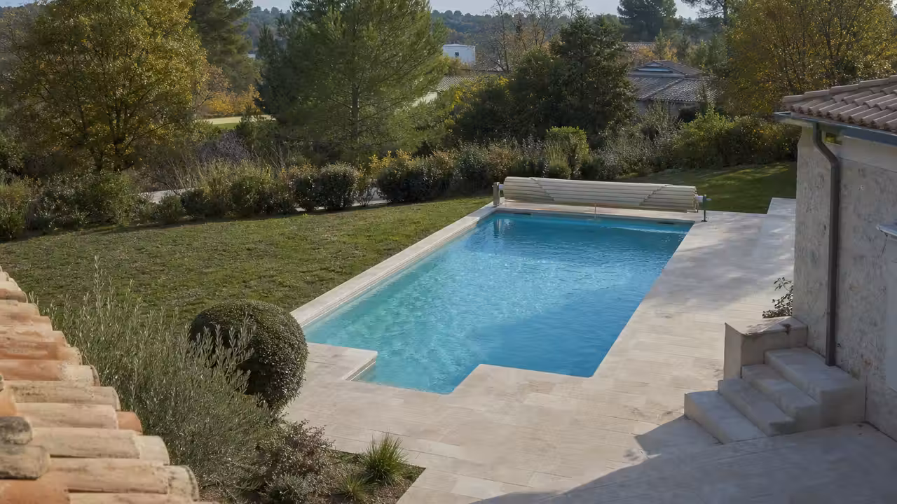 Piscine enterrée vue en plongée dans un jardin résidentiel, avec terrasse minérale et végétation en périphérie
