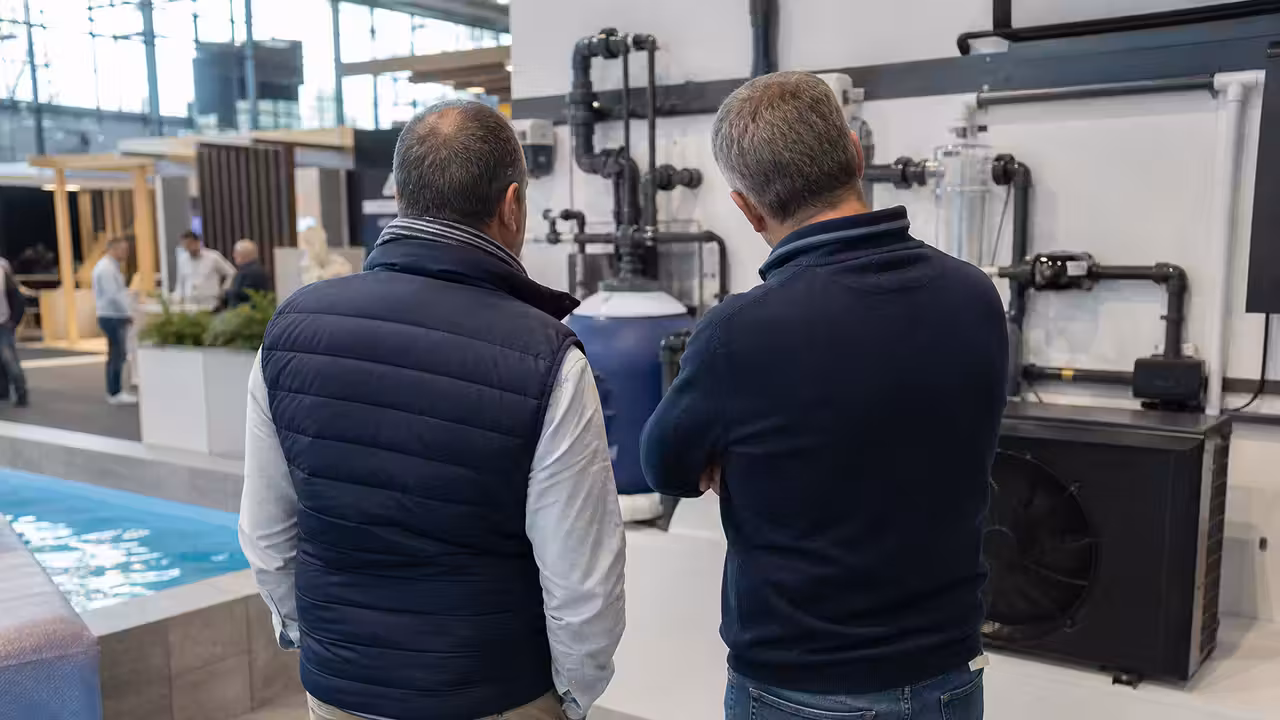 Allée de salon professionnel présentant des équipements de filtration et de chauffage pour piscine sur des stands lumineux