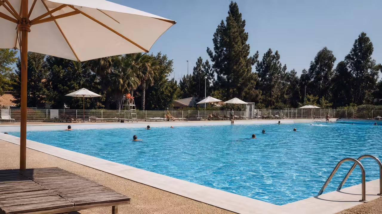 Bassin extérieur d’une piscine municipale avec baigneurs, maîtres-nageurs et espaces ombragés en été