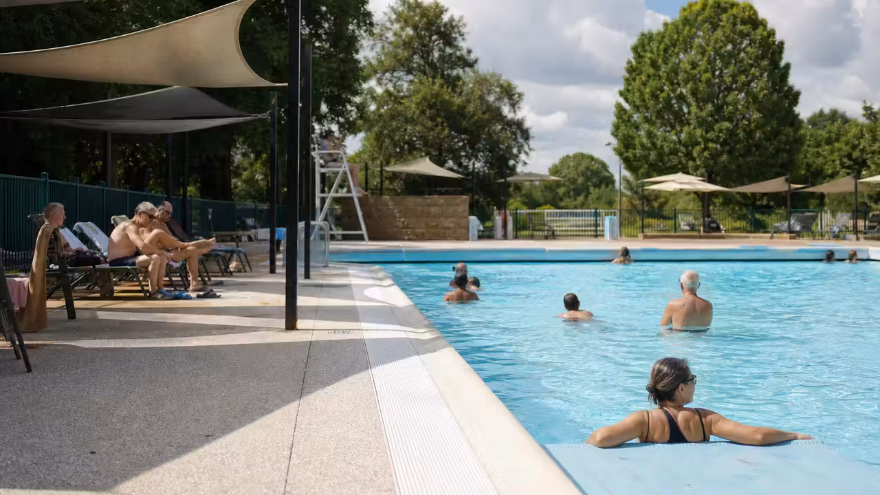 Bassin extérieur municipal avec zones ombragées et baigneurs profitant d’une journée d’été changeante