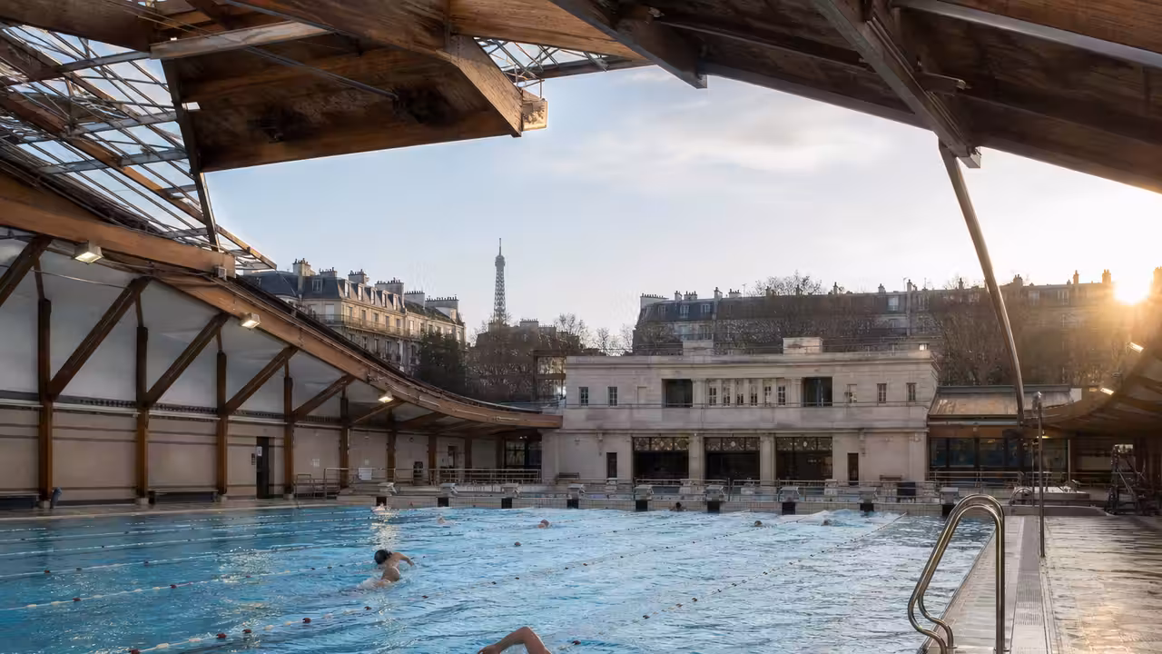 Bassin de nage de 50 mètres sous un toit ouvrant dans une piscine publique parisienne historique.