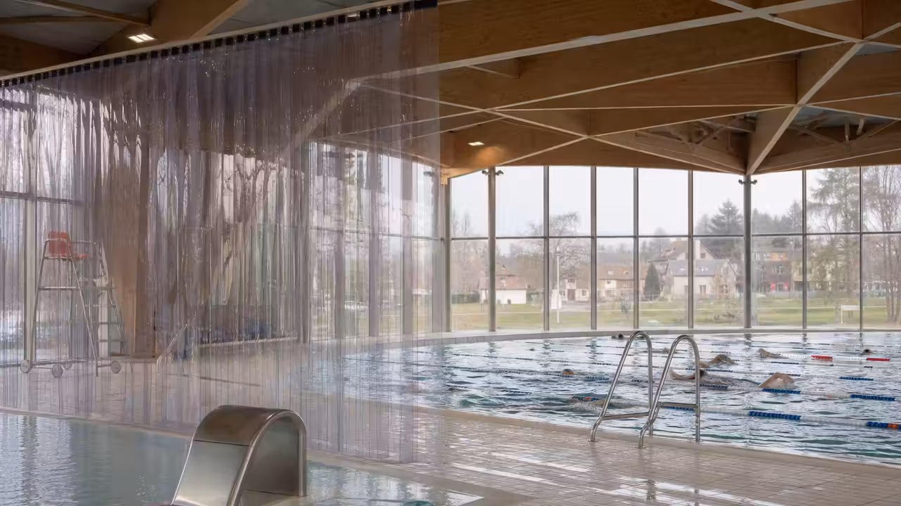 Rideau transparent à lanières PVC séparant deux espaces de baignade dans une piscine publique lumineuse