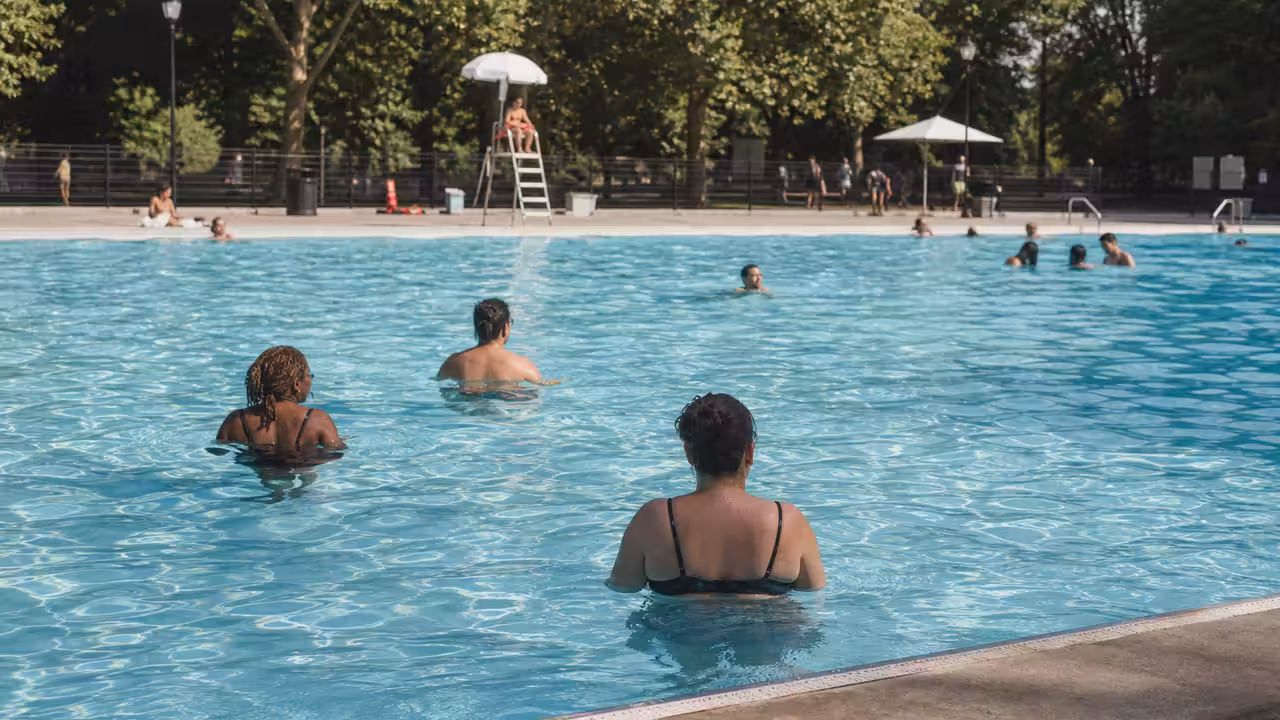 Bassin extérieur surveillé dans un parc public, avec familles et végétation estivale en arrière-plan