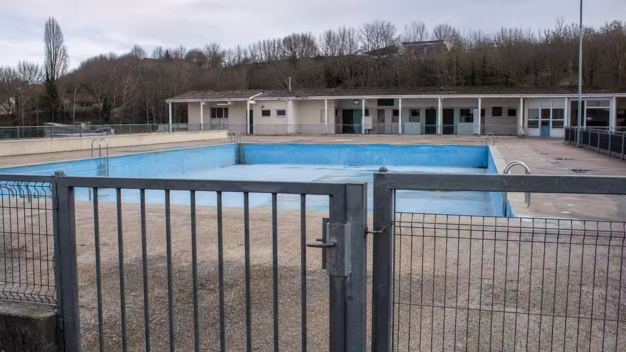 Grille fermée devant un bassin municipal extérieur vide, illustrant l’attente d’un nouvel équipement aquatique