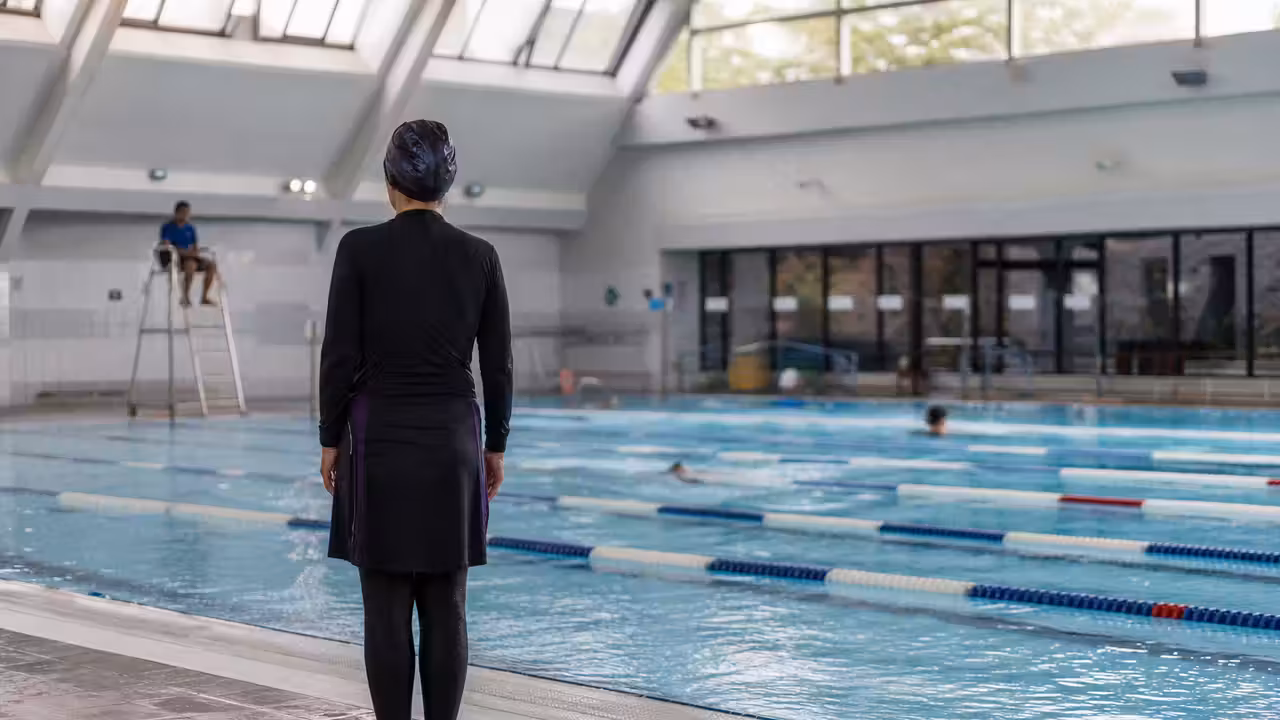 Nageuse portant une tenue de bain couvrante au bord d’un bassin municipal lumineux et surveillé