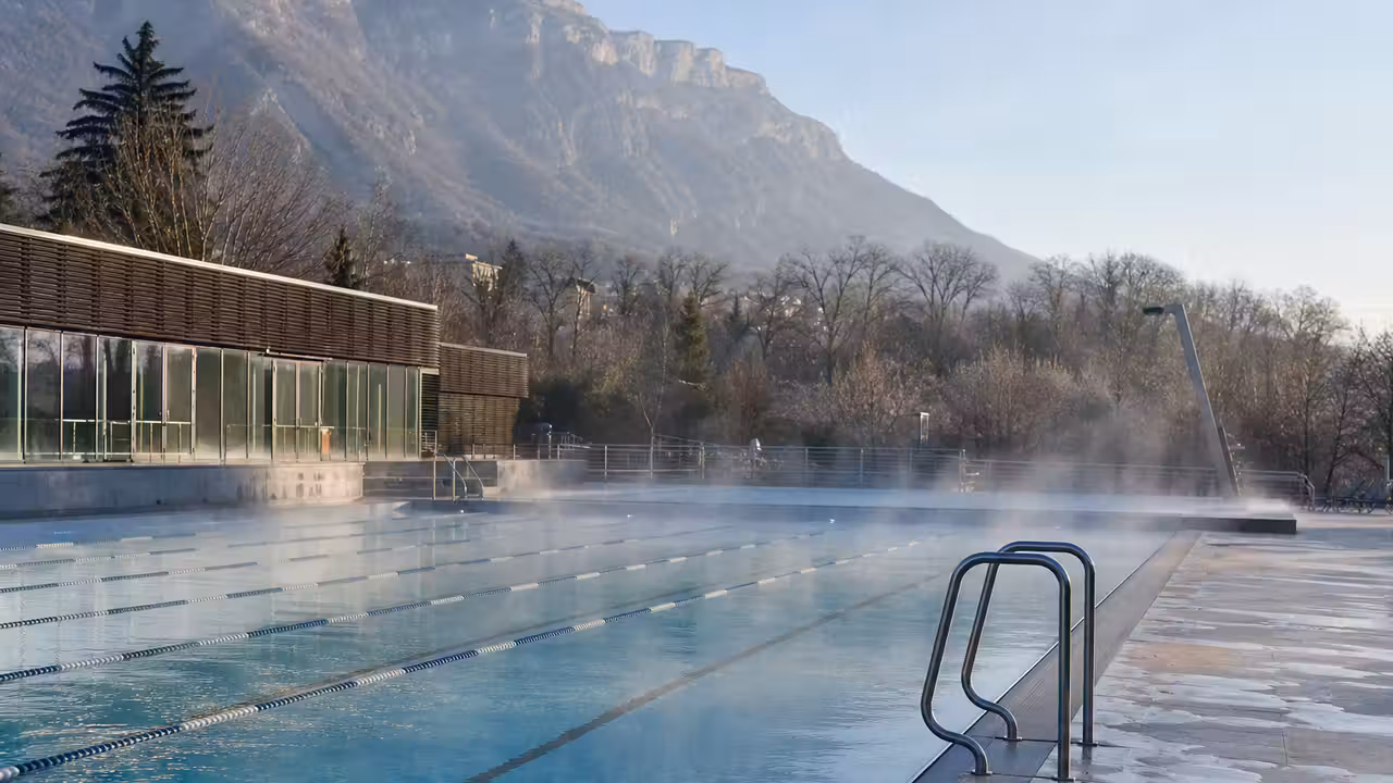 Bassin extérieur d’un centre aquatique avec lignes de nage, vapeur légère et montagnes en arrière-plan