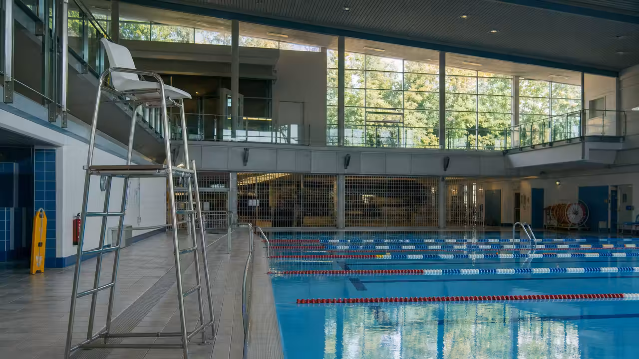 Agents d’un centre aquatique municipal examinant un planning près de lignes d’eau encore vides.