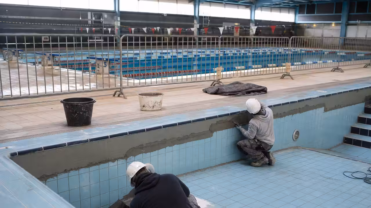 Bassin de natation couvert en rénovation avec zone de chantier isolée et lignes d’eau visibles en arrière-plan