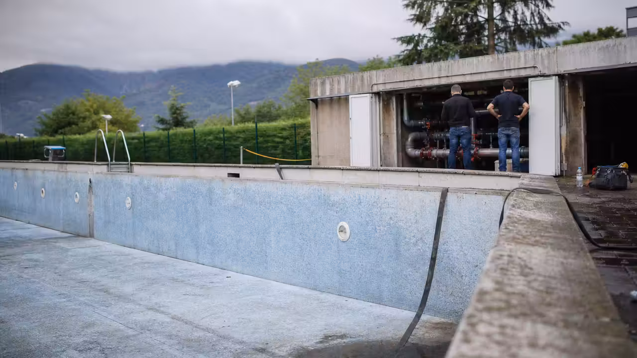 Bassin extérieur municipal vide, avec plages humides et local technique fermé lors de travaux de réparation