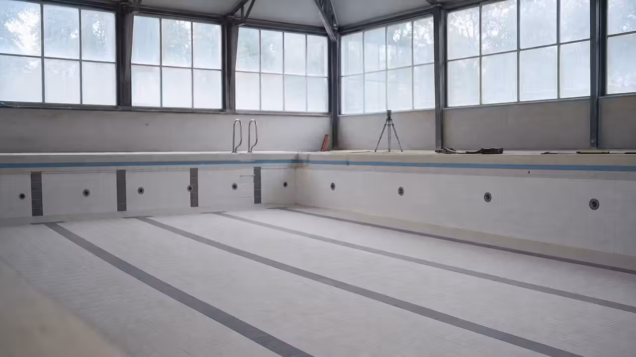 Bassin de piscine publique vidé, avec fissures visibles au sol et sur une paroi en béton