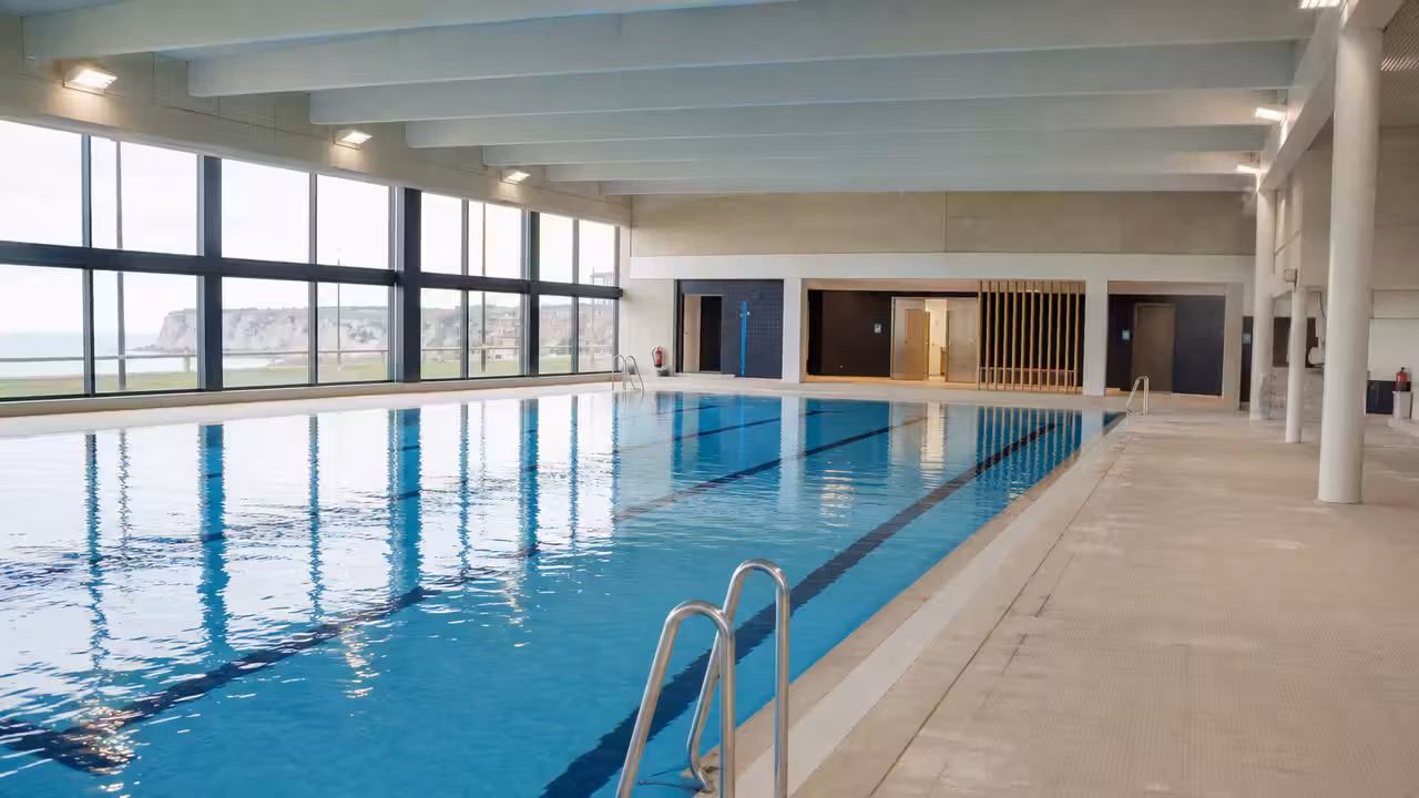 Bassin intérieur rénové d’une piscine municipale avec lignes d’eau, vestiaires lumineux et baigneurs au loin