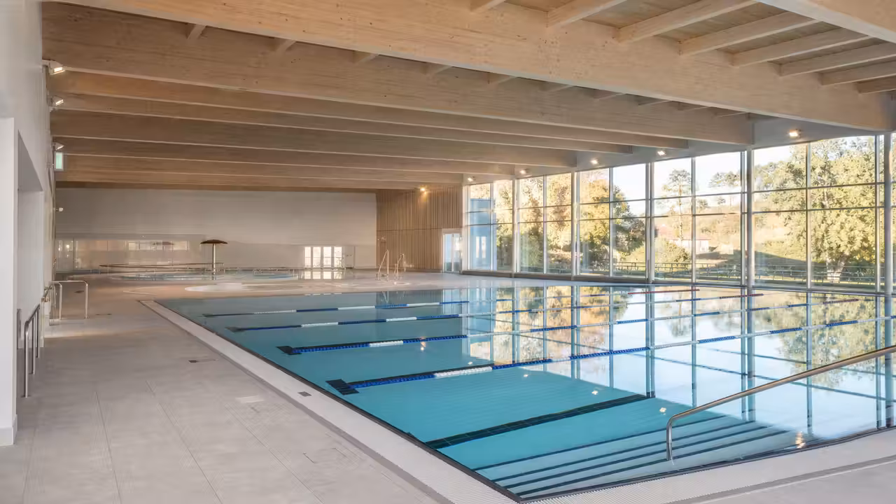 Bassin intérieur lumineux d’un centre aquatique municipal avec lignes d’eau et grandes baies vitrées
