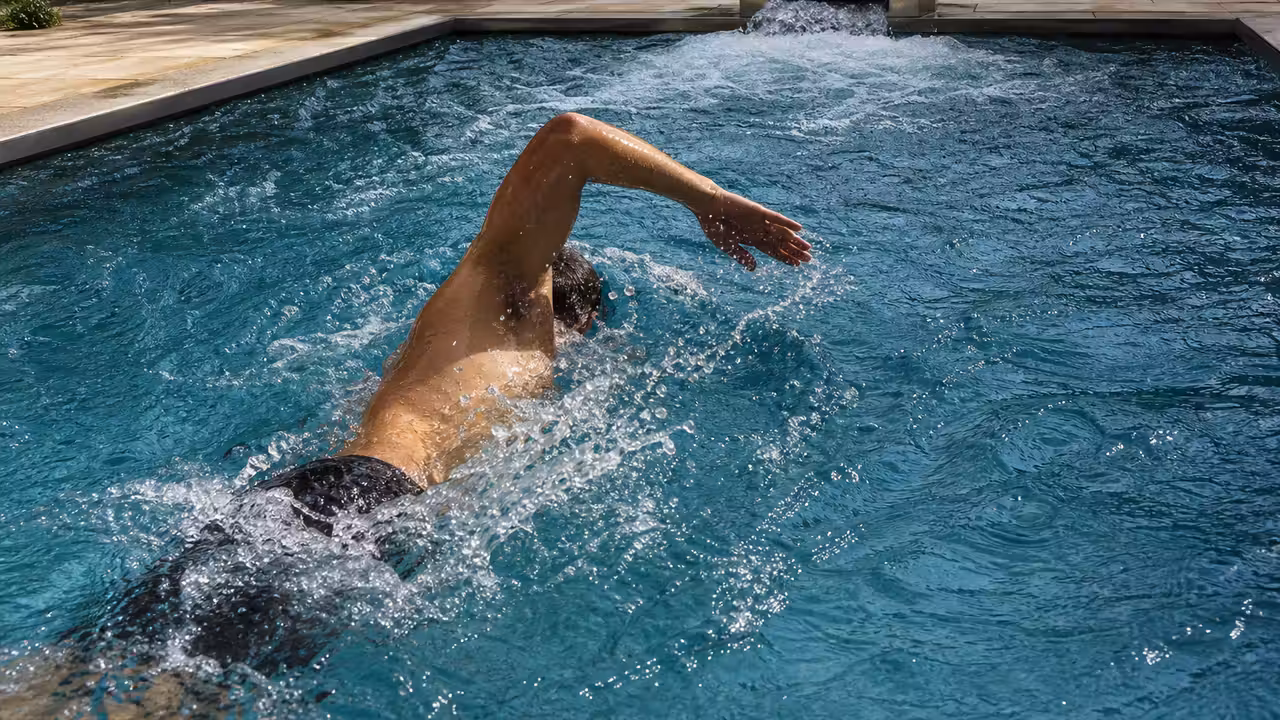 Nageur adulte utilisant un appareil de nage à contre-courant fixé sur la margelle d’une piscine privée