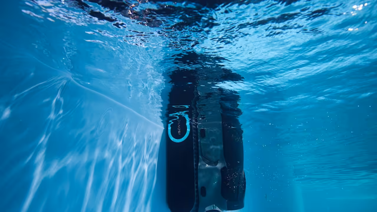 Robot de piscine sans fil nettoyant le fond d’un bassin contemporain aux parois en mosaïque bleue.