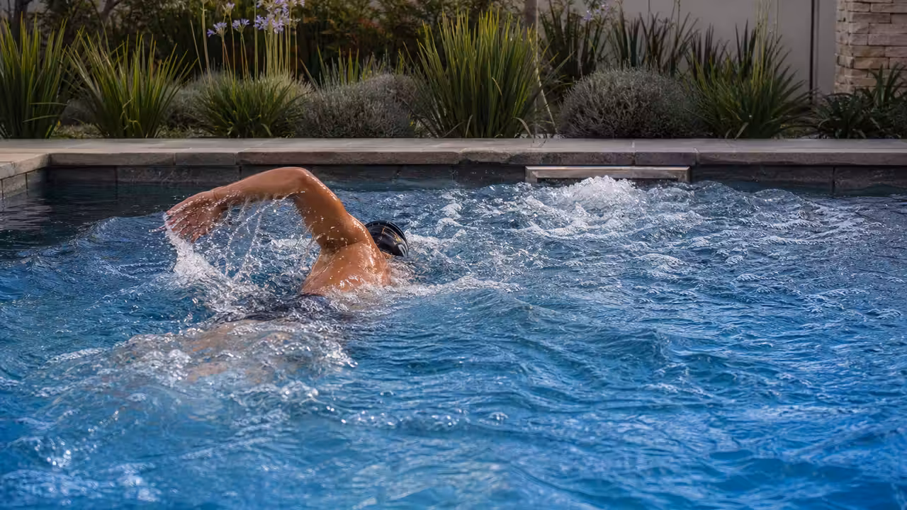 Nageur adulte de dos s’entraînant face à un puissant courant dans une piscine privée contemporaine