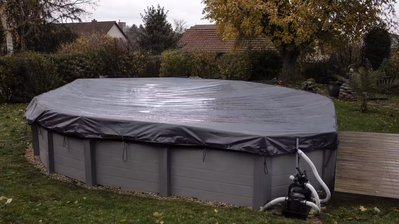Piscine hors-sol couverte dans un jardin à l’automne, avec feuilles au sol et matériel d’hivernage