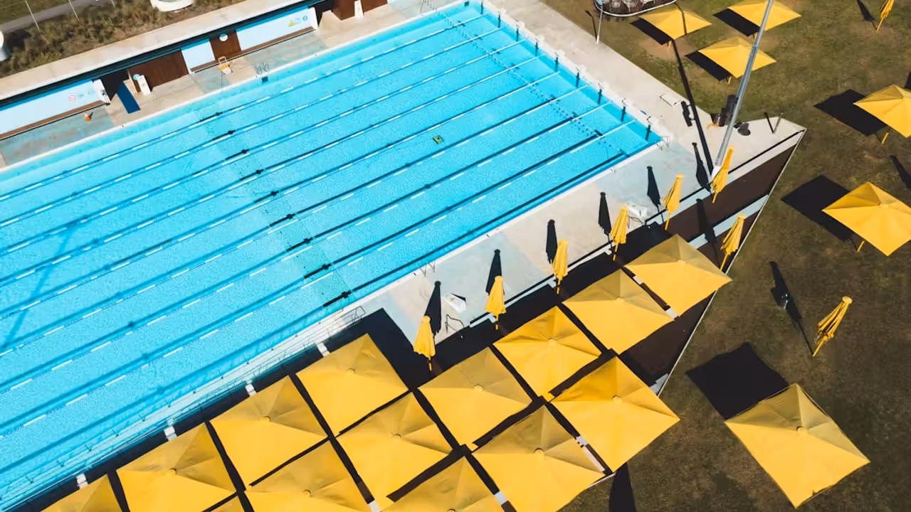 Bassin intérieur rénové d’une piscine municipale avec lignes d’eau, vestiaires lumineux et baigneurs de dos