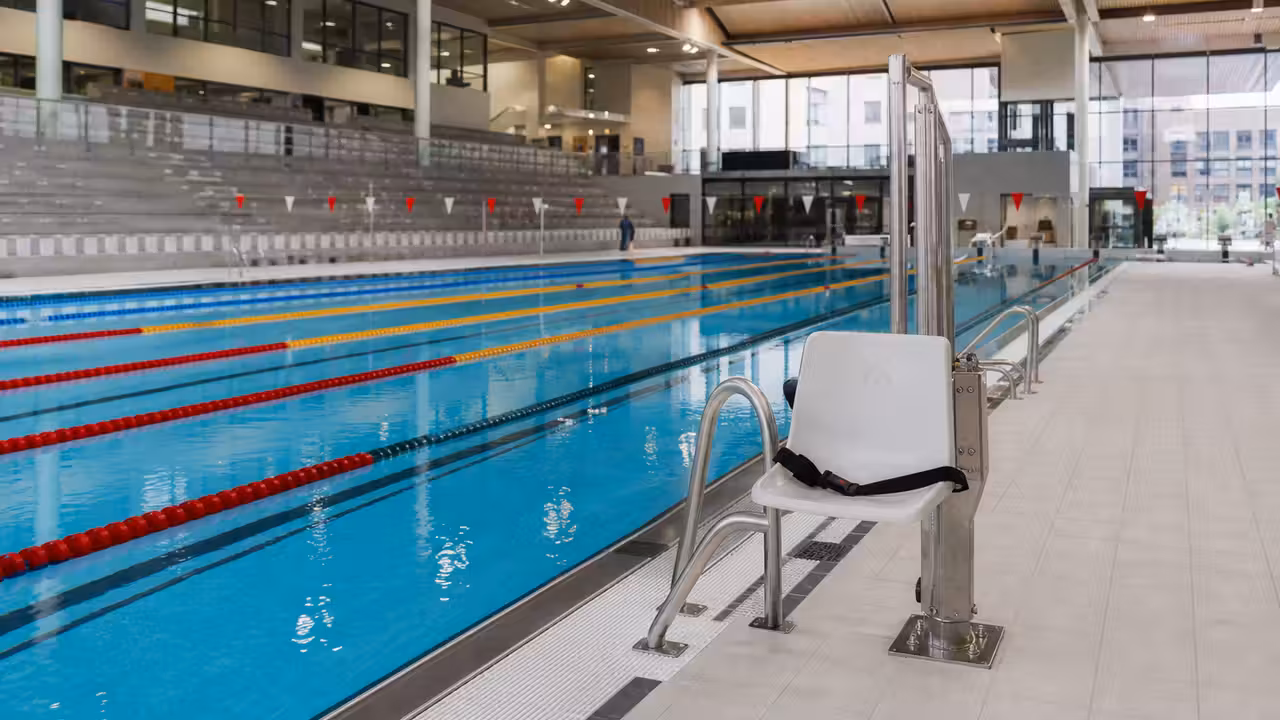 Bassin de natation de 50 mètres dans un centre aquatique moderne, avec lignes d’eau et gradins.