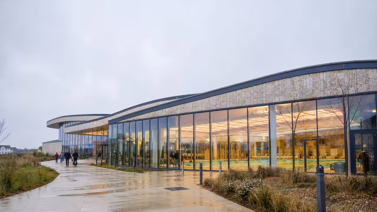 Vue extérieure d’un centre aquatique municipal moderne avec bassins visibles derrière de larges baies vitrées